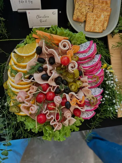 A beautifully arranged charcuterie platter featuring rolled cold cuts, olives, and fresh fruits like dragon fruit and orange slices. A non-vegetarian delight for any celebration.