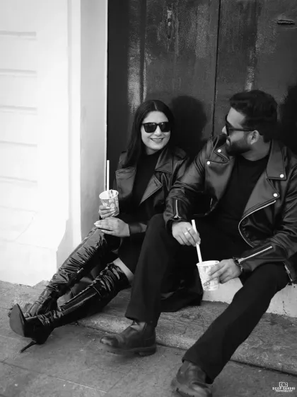 A candid black and white shot of the couple relaxing on some steps, dressed in matching leather jackets and enjoying a drink, showing a cool and casual side.