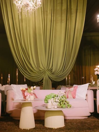 A beautiful lounge setup featuring modern pink sofas under dramatic olive green drapes and sparkling crystal chandeliers.