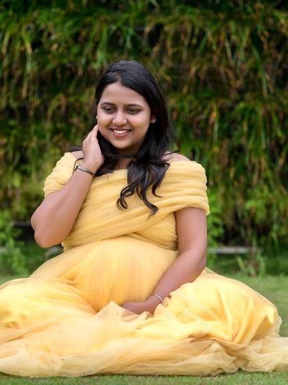 A happy and relaxed outdoor maternity shot. The soft, flowy yellow fabric of this off-shoulder gown drapes beautifully for seated portraits, creating a cheerful and bright image.