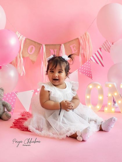 This little girl's smile lit up the entire studio during her "Pretty in Pink" first birthday session. The soft pink backdrop, balloons, and light-up 'ONE' sign created a perfectly sweet and celebratory atmosphere.