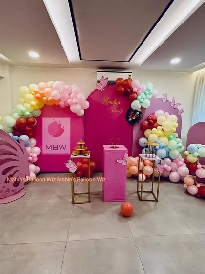 A vibrant and modern butterfly-themed fifth birthday. The bold pink backdrops are complemented by a rainbow balloon garland and a large, laser-cut butterfly wing prop.