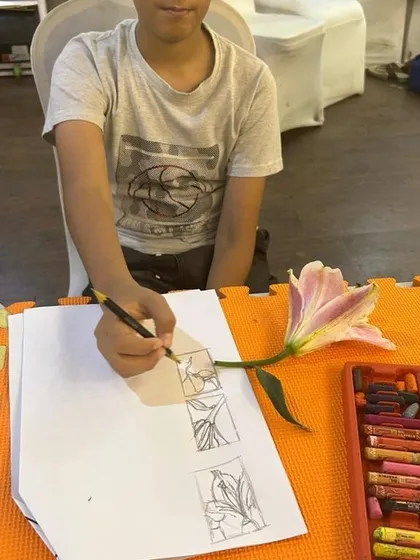 The first step in our still life session: observation and sketching. This student is studying a lily to understand its form before starting his large-scale floral artwork.