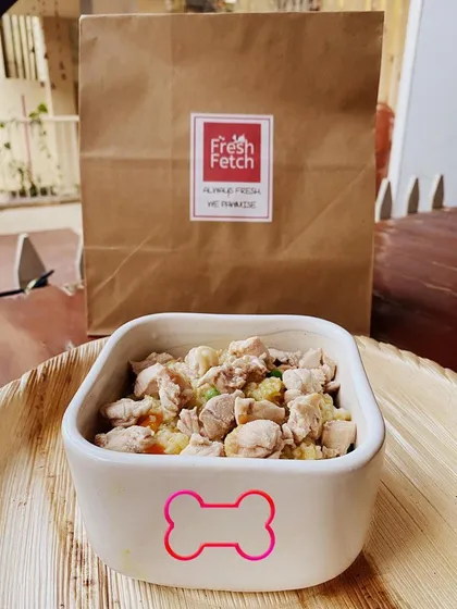 A bowl of our 'Bow Chicky Bow Chow' ready to be served, with its eco-friendly delivery bag in the background. It's a favorite among our furry customers.