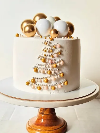 An elegant and minimalist Christmas cake. The simple white design features a Christmas tree made of gold and white sugar pearls, topped with a star.