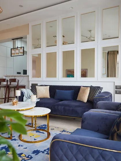 This living room showcases a bold yet warm palette of white, beige, and blue, with subtle gold highlights. The mirror paneling with intricate moulding visually expands the area, creating a space that exudes both luxury and functional beauty.