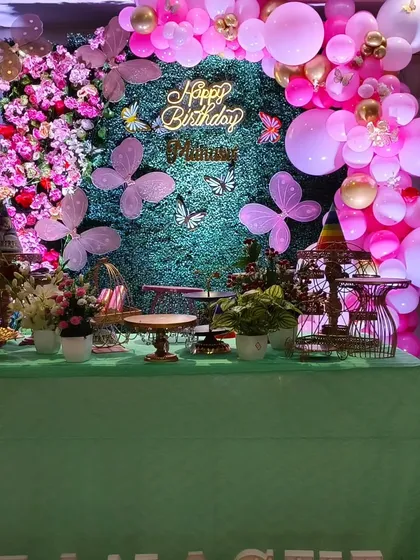 I created this enchanting butterfly garden theme using a lush green hedge wall as the base. The design features a custom neon "Happy Birthday" sign, delicate butterfly cutouts, and an organic balloon garland in vibrant pinks and gold.