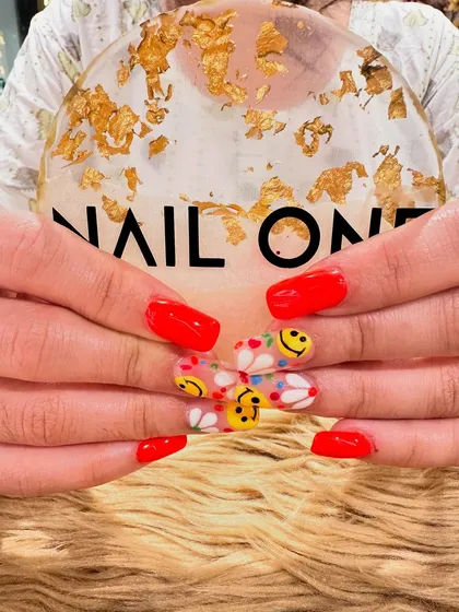 A close-up of the smiley face and daisy nail art. The clear base on the accent nails makes the colorful designs pop, showcasing our skill with fine-line brushwork.