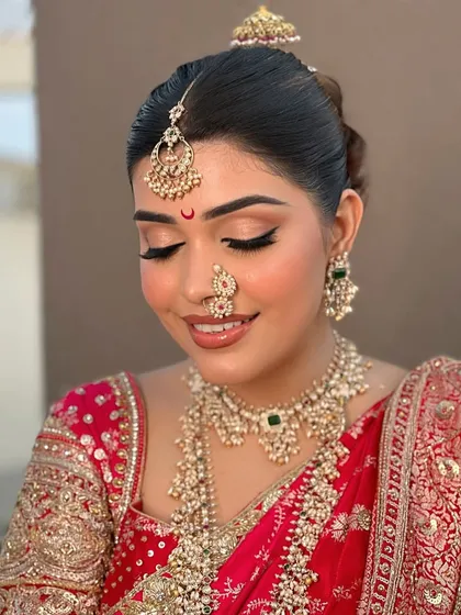 A beautiful close-up of a bride adorned in layers of tradition. This look features a polki choker, a long rani haar, a delicate nath, and a borla-style maang tikka, creating a rich and complete bridal profile.