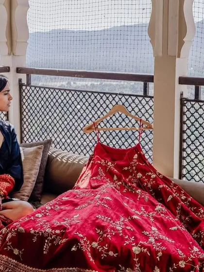 The bride sits by the window with her lehenga, a moment of anticipation before the ceremonies begin.