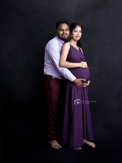 A classic full-length studio portrait of a couple against a solid black background. This timeless setup puts all the focus on the parents-to-be.