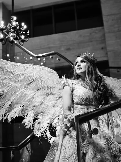 A dramatic black and white photo of the bride on a grand staircase, her angel wings spread wide, creating a powerful and artistic image.