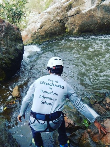 A graduate ready for the next challenge, geared up with a harness and helmet by the stream.