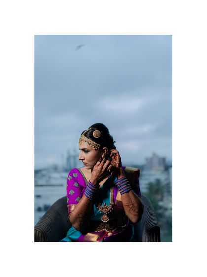 A South Indian bride adjusts her earring against a city skyline. This portrait captures her elegance and the urban setting of her wedding.