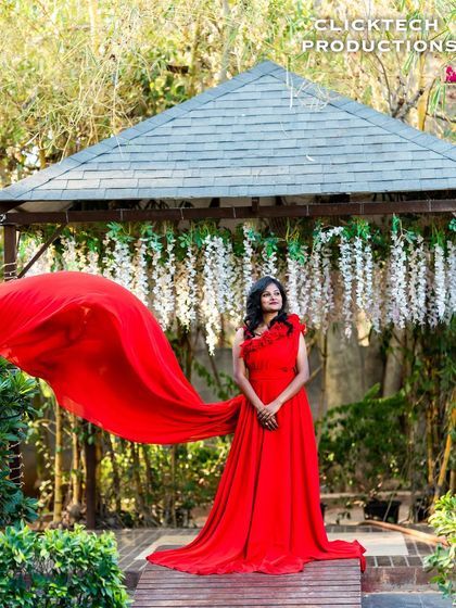 A beautiful solo portrait of the bride-to-be in a flowing red gown, set against a gazebo with hanging white flowers, creating a garden fairy-tale look.