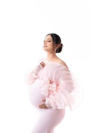 A moment of pure bliss. The mother-to-be cradles her bump, her expression full of love, wearing a beautiful pink gown with statement organza sleeves.