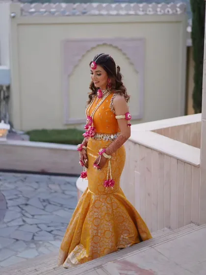 For a sunny Haldi ceremony, I designed this vibrant marigold Banarasi mermaid skirt paired with a hand-embroidered blouse. The fish-cut silhouette is a modern twist on traditional Haldi attire, and the mirror-work tassels add a playful, festive touch.