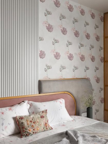 The bed's headboard is a study in contrasts, with a soft pink frame, a grey upholstered section, and a fluted white panel beside it. The floral wallpaper enhances the room's tranquil, pastel aesthetic.