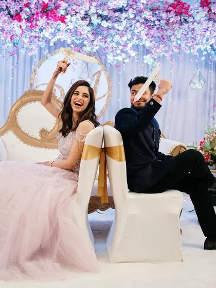 A wider angle of the shoe game, showing the beautiful stage decor and the couple's joyful participation in this classic engagement party activity.