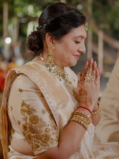 A close-up of the mother of the groom during the wedding ceremony. Her serene expression is complemented by the exquisite craftsmanship of her ivory saree and traditional jewelry.