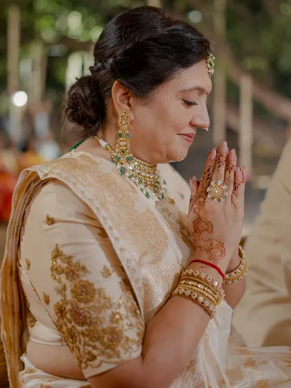 A close-up of the mother of the groom during the wedding ceremony. Her serene expression is complemented by the exquisite craftsmanship of her ivory saree and traditional jewelry.