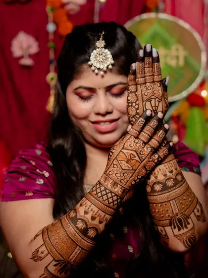 A lovely photo of a bride during her mehendi ceremony. Her hands are adorned with a dense floral and paisley pattern, covering her hands and forearms completely.