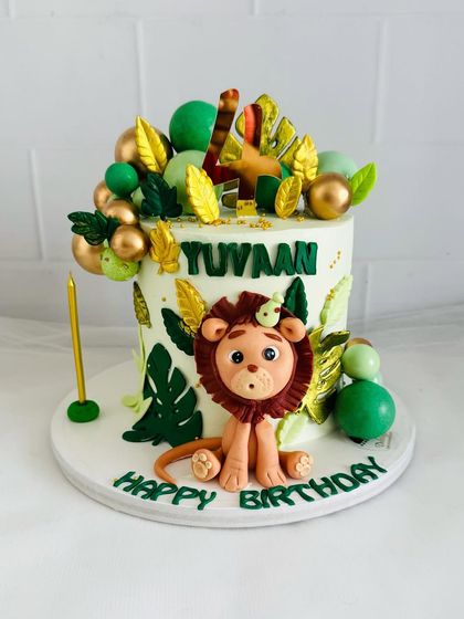 A vibrant jungle-themed cake with a cute fondant lion, tropical leaves, and golden accents.