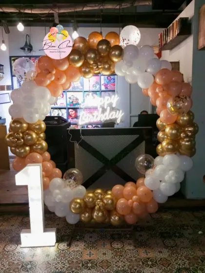 A stylish balloon ring in peach, white, and gold for a first birthday, complete with a marquee number.