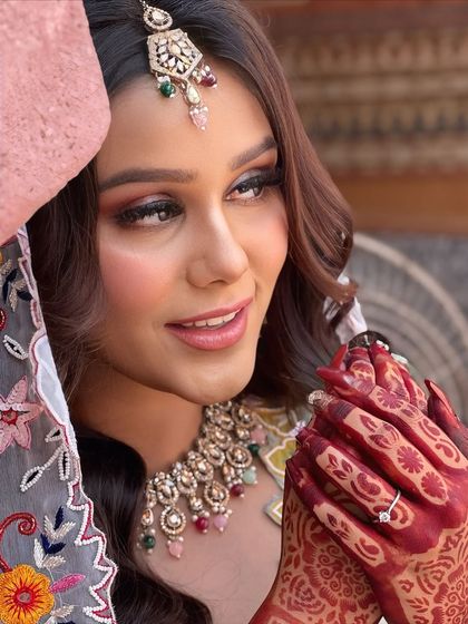 A playful and happy shot that showcases the bride's radiant smile and detailed henna. The makeup is designed to be long-lasting and picture-perfect for daytime events.