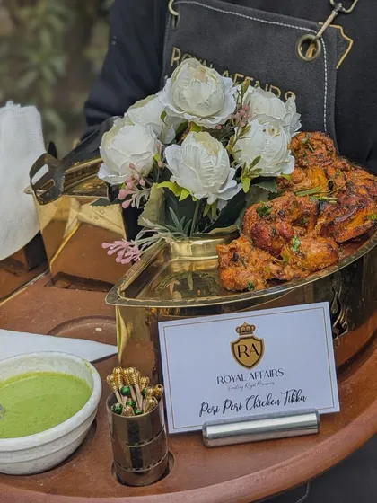 I take pride in the quality and presentation of each dish. Here, my staff serves freshly grilled Peri Peri Chicken Tikka, presented in a beautiful brass boat-shaped dish with a side of cooling mint chutney, ready to be passed around to guests.