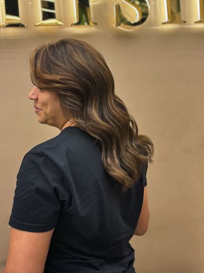 A side view of a client's hair after a color service that provides excellent grey coverage. The soft waves and rich color create a timeless and elegant style.