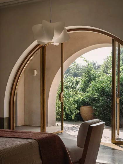 A bedroom in the Dua Villa opens directly onto the landscape through brass-framed arched doors. This seamless transition is central to our philosophy of creating homes that live in harmony with nature.
