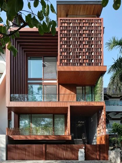 The 'Vrinda' residence features an intricate wooden jaali screen on its facade. This element provides privacy and shade while casting beautiful patterns of light, blending traditional Indian craftsmanship with contemporary design.