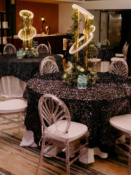 Glamorous guest seating with black sequin tablecloths, modern illuminated centerpieces, and clear acrylic chairs for a sleek, contemporary look.