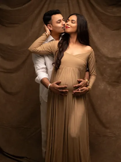 A tender and romantic studio portrait. The partner's gentle kiss and embrace create a beautiful, intimate moment for this expecting couple.