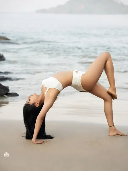 A creative and athletic pose on the beach, showcasing the model's flexibility. The backbend pose creates a beautiful arch against the backdrop of the ocean.