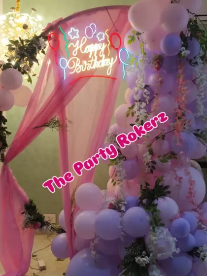 A photo of the romantic birthday setup, showing the combination of the balloon-and-flower-draped ring with a colorful "Happy Birthday" neon sign.