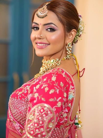 A smiling bride in a bright pink lehenga, showcasing a beautiful gold and green jewellery set. I offer a variety of jewellery options to match your rental outfit.