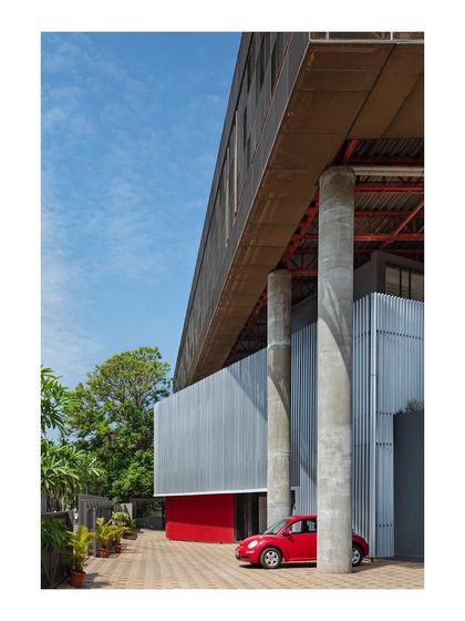 The "Hoverspace" office extension is supported by massive concrete columns, allowing the new volume to float above the ground. A red car provides a pop of color and a sense of scale.