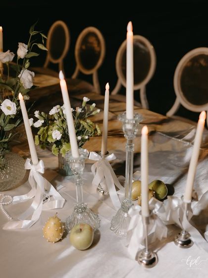 A romantic, candlelit tablescape from a Goa dinner. The table is adorned with white flowers, fresh green apples, and strings of pearls, creating a soft and ethereal look.