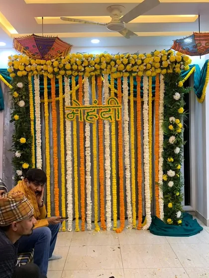 This is a classic Mehndi backdrop we set up in a client's home. It features strings of fresh yellow, white, and orange marigolds with a "Mehndi" sign, perfect for traditional pre-wedding functions in a compact space.