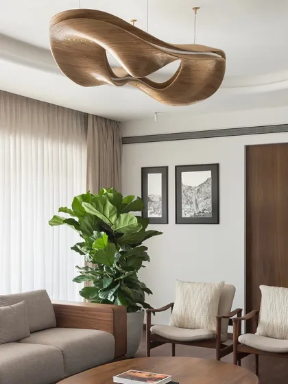 Lighting is more than just illumination; it's the jewelry of a room. This sculptural wooden chandelier in the West Coast Residence serves as a central art piece, anchoring the living space with its organic form and warm, ambient glow.