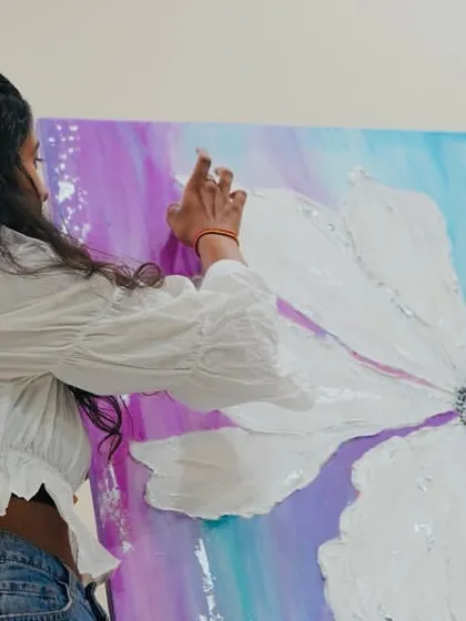 Here I am working on a large floral piece, using a spray bottle to blend the background colors. The white textured flower stands out against the vibrant purple and blue, symbolizing purity and growth amidst life's complexities.