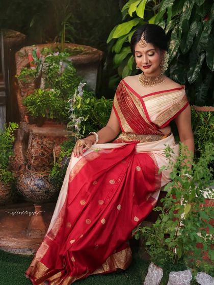 Portraits from a makeup shoot, showcasing a model in a classic red and cream saree. The images highlight the flawless makeup and traditional styling in a beautiful garden setting.