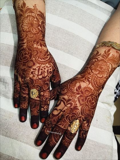 A close-up of the rich henna stain, showcasing the bride's name delicately woven into the floral design on her palm.