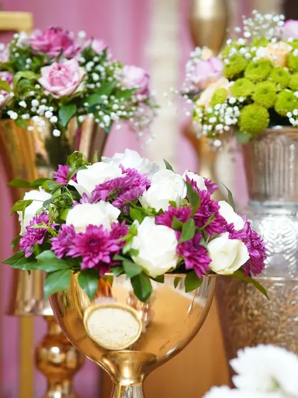 Detailed floral arrangements in polished brass vases. We focus on color coordination, mixing white and purple flowers with pops of green to create visually appealing centerpieces.