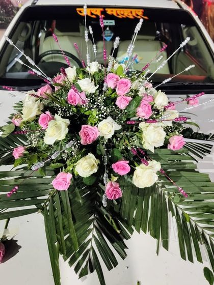 This wedding car decoration features a beautiful bouquet of pink and white roses with baby's breath, accented with decorative silver sticks and palm leaves for a touch of flair.