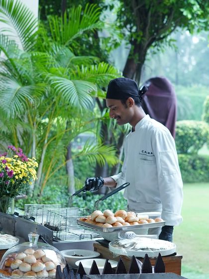 A chef at a live cooking station, preparing fresh food for guests at an outdoor event. Live kitchens add an element of theater and ensure the food is served hot and fresh.
