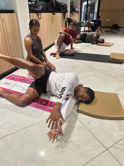 A supine twisting pose for a tennis player, focusing on hip and spinal mobility. I am guiding the student to ensure the stretch is effective and safe, helping to release tension accumulated from repetitive athletic movements.