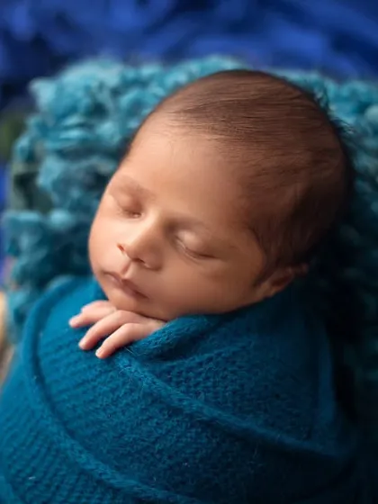 A close up shot of a baby boy nestled in a basket. The rich blue tones of the wrap and the fluffy texture of the liner create a beautiful, cozy image.
